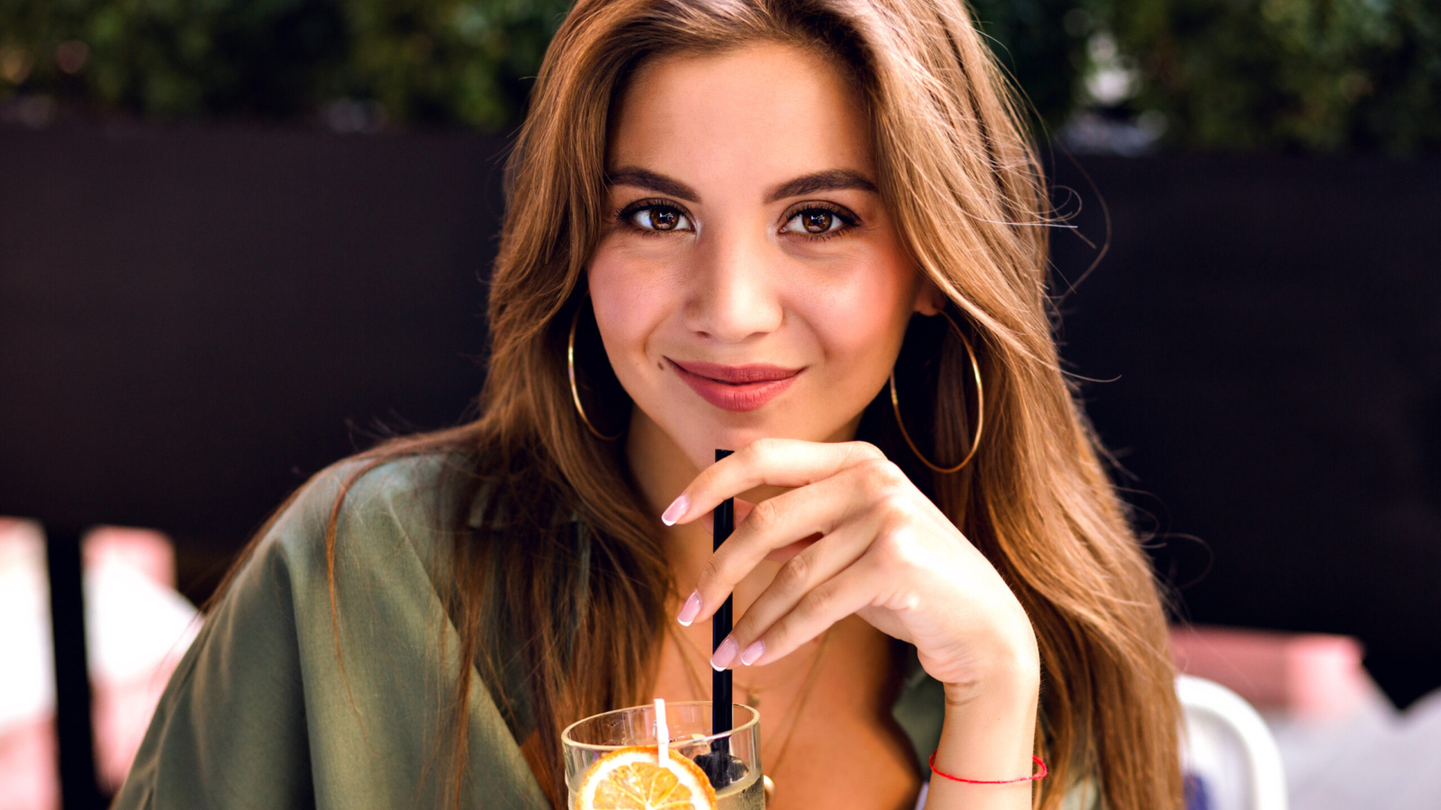 Close up image of pretty brunette woman drinking tasty lemonade and looking on camera, enjoying time at city terrace, warm summertime, natural beauty.