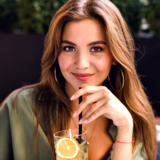 Close up image of pretty brunette woman drinking tasty lemonade and looking on camera, enjoying time at city terrace, warm summertime, natural beauty.