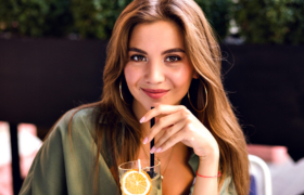 Close up image of pretty brunette woman drinking tasty lemonade and looking on camera, enjoying time at city terrace, warm summertime, natural beauty.