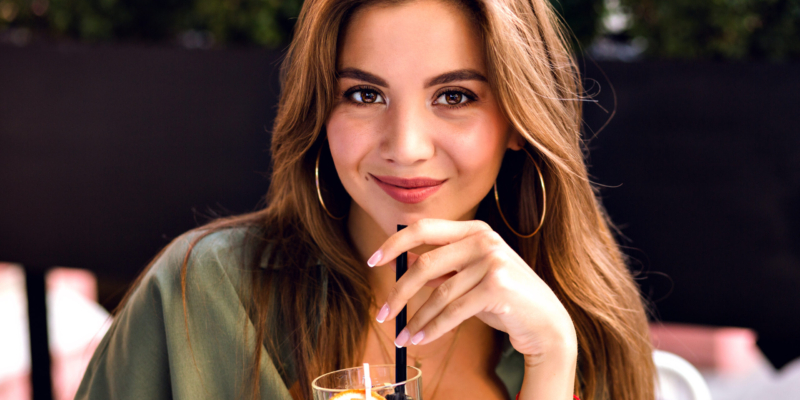 Close up image of pretty brunette woman drinking tasty lemonade and looking on camera, enjoying time at city terrace, warm summertime, natural beauty.