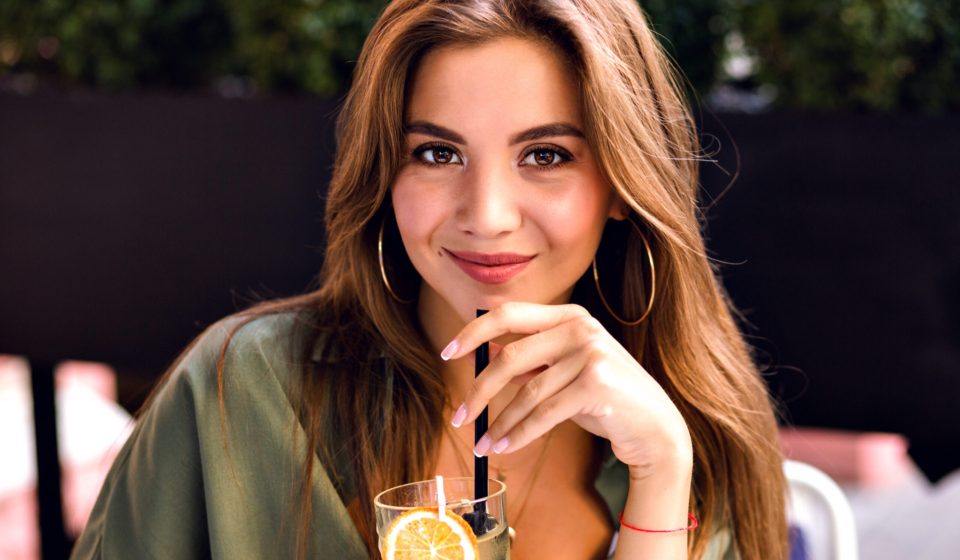 Close up image of pretty brunette woman drinking tasty lemonade and looking on camera, enjoying time at city terrace, warm summertime, natural beauty.