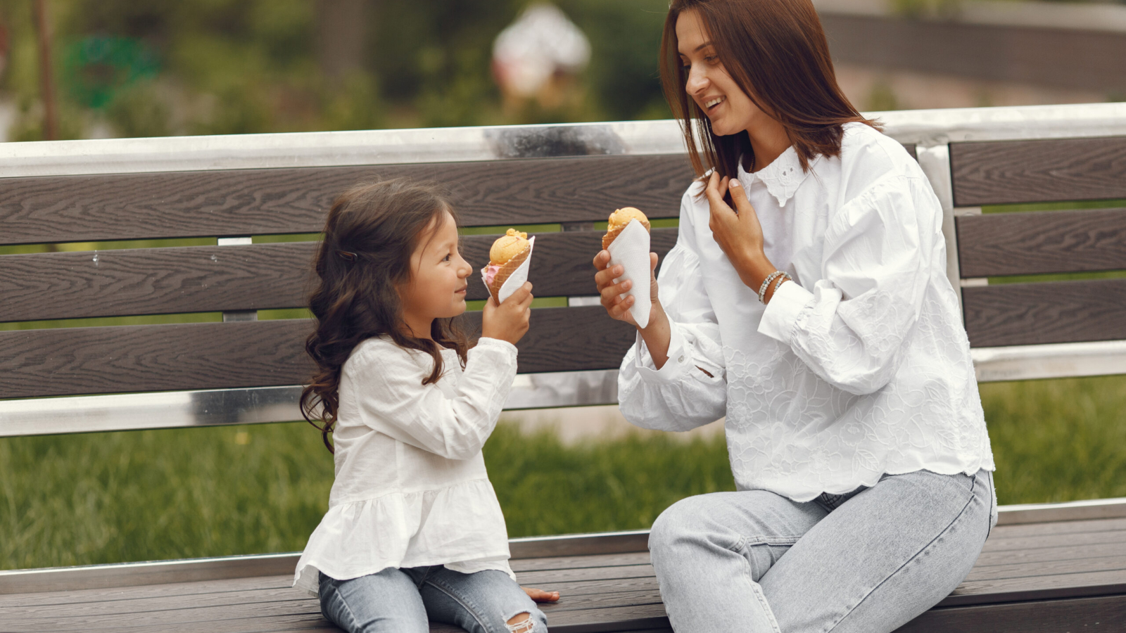 Family in a city. Little girl eats ice cream. Mother with daughter sitting on a bench.