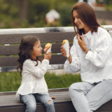 Family in a city. Little girl eats ice cream. Mother with daughter sitting on a bench.