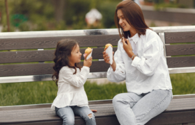 Family in a city. Little girl eats ice cream. Mother with daughter sitting on a bench.